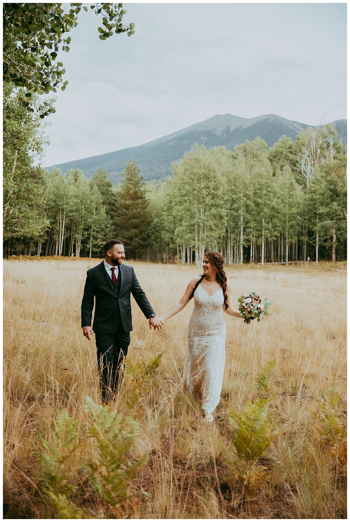bride and groom holds hands as they walk through a meadow in flagstaff forests