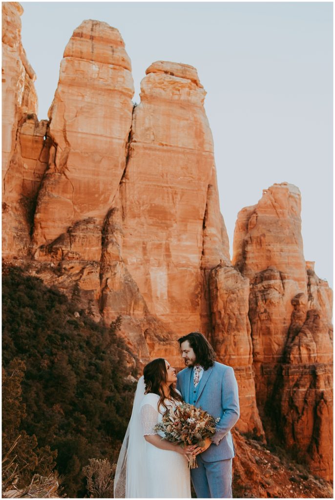 bride and groom standing at the top of Cathedral Rock with their hands on their bouqeut