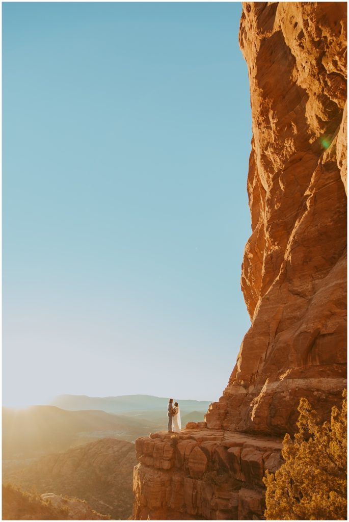 bride and groom stands on a cliff at Cathedral Rock during sunset