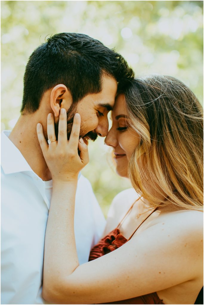 man and woman touches foreheads as woman holds man's face while wearing wedding ring