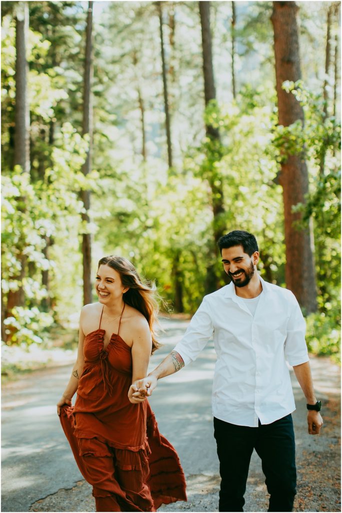 Couple laughs as they walk down a paved road in a forested area in Arizona
