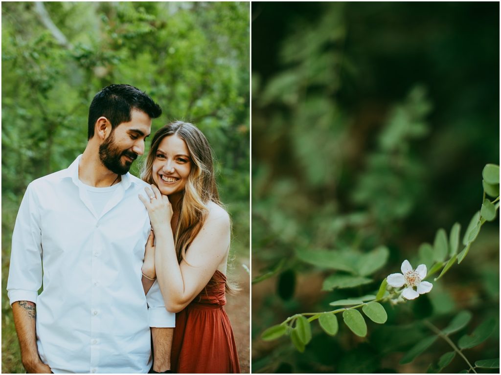 woman smiles while leaning on man's shoulder in front of greenery.