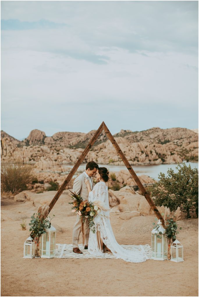 bride and groom kiss beneath an arch at a boho wedding at Watson Lake in Prescott, Arizona