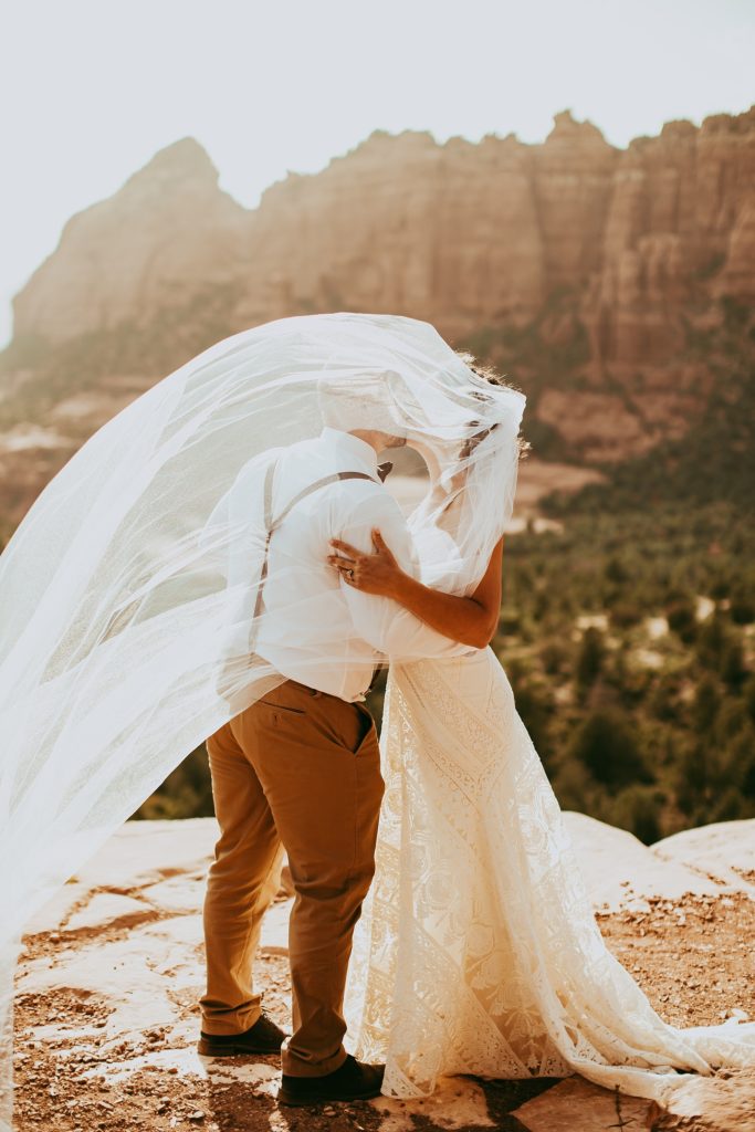 bride and groom kiss as the veil covers their heads and hides their faces with Sedona's iconic mountain scenery in the background