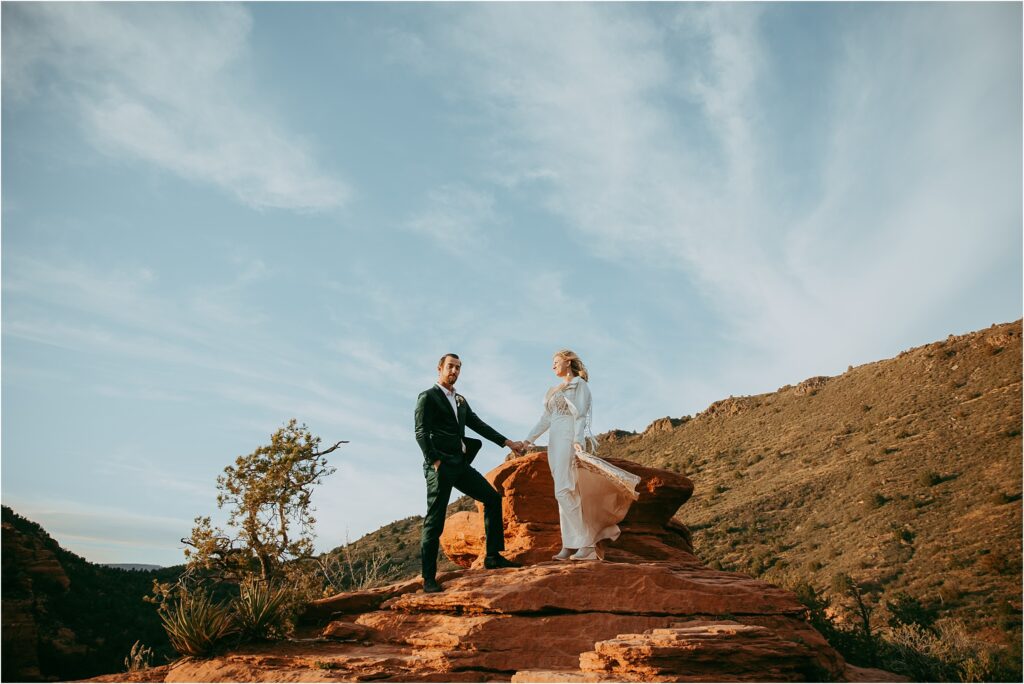 Bride and groom holds hands on red rock in Sedona
