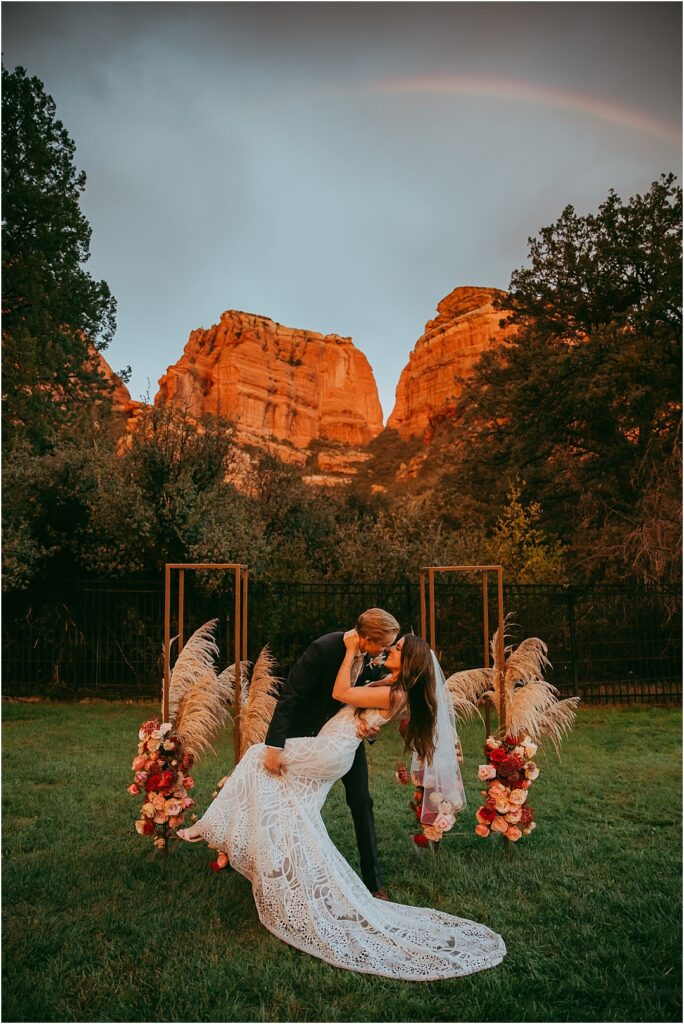 bride and groom kiss beneath a rainbow and iconic Sedona red rocks