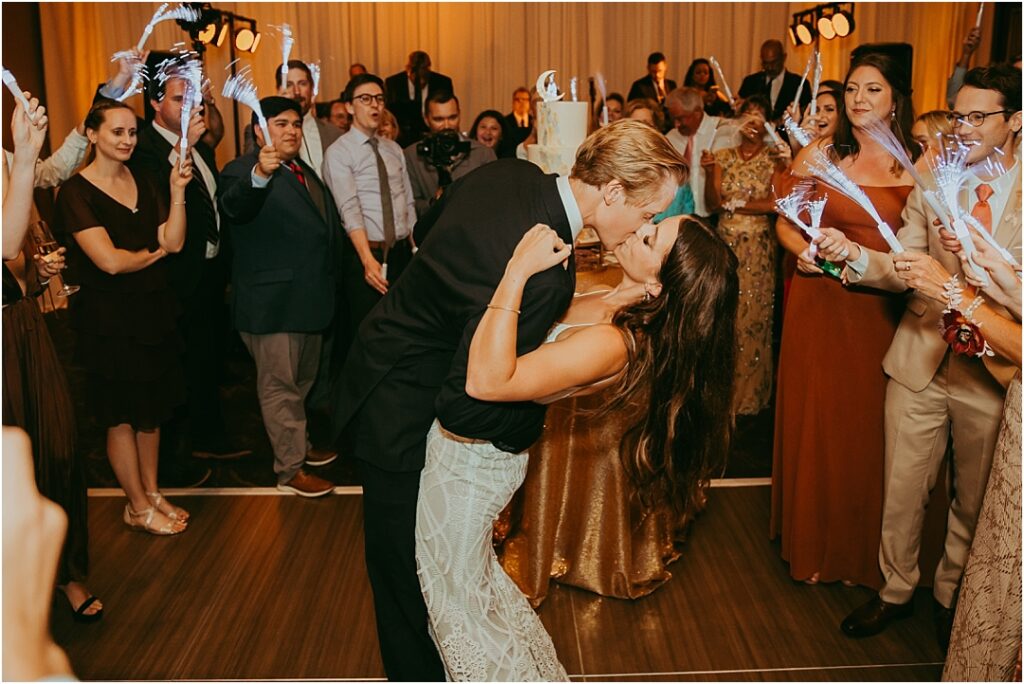 groom bends bride for kiss in front of reception guests on dance floor