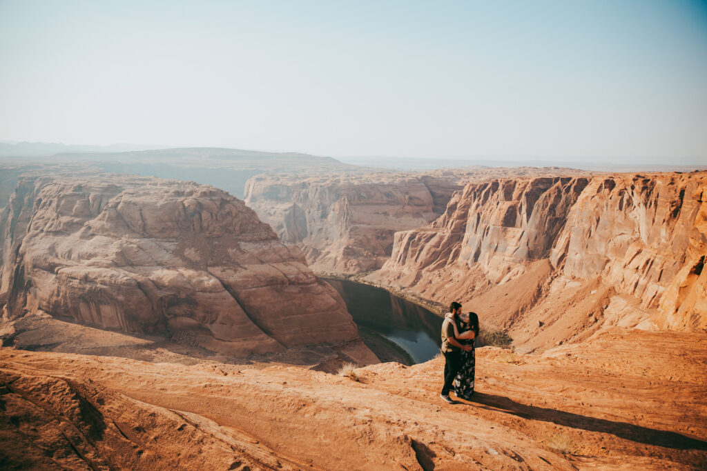 a man and woman hold each other on a cliff in front of Horseshoe Bend