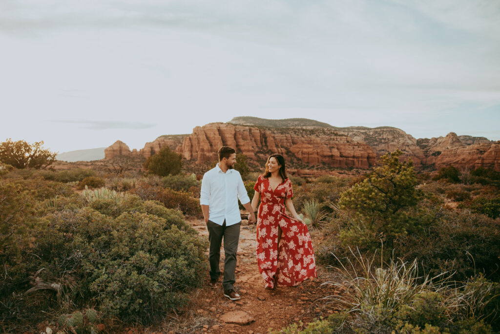A man and woman walk with each other while smiling for their Sedona engagement photos on top of Doe Mountain