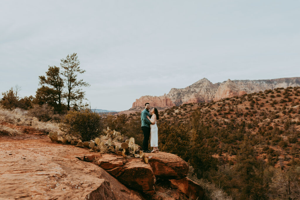 A man smiles and looks toward the camera while holding his fiance during a Sedona engagement shoot at Munds Wagon.