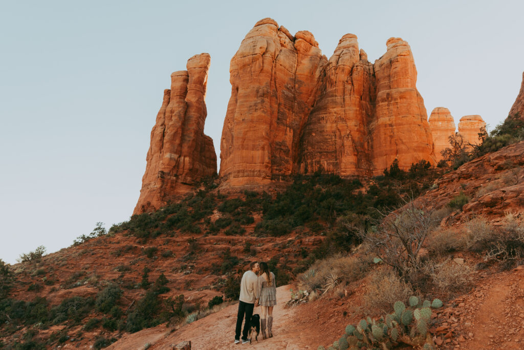 a couple hikes with their dog up to Cathedral Rock wearing matching beige colors for their Sedona engagement photos
