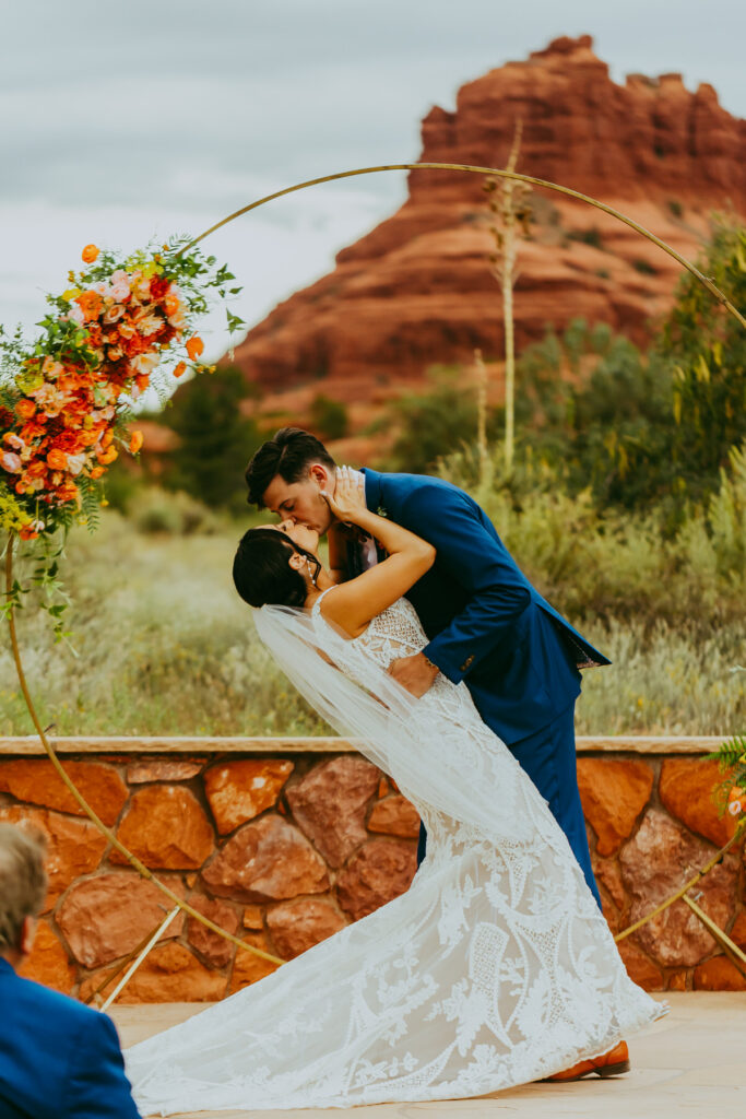 groom dips bride as he leans in for a kiss at red agave adventure resort with beautiful sedona red rock backdrop