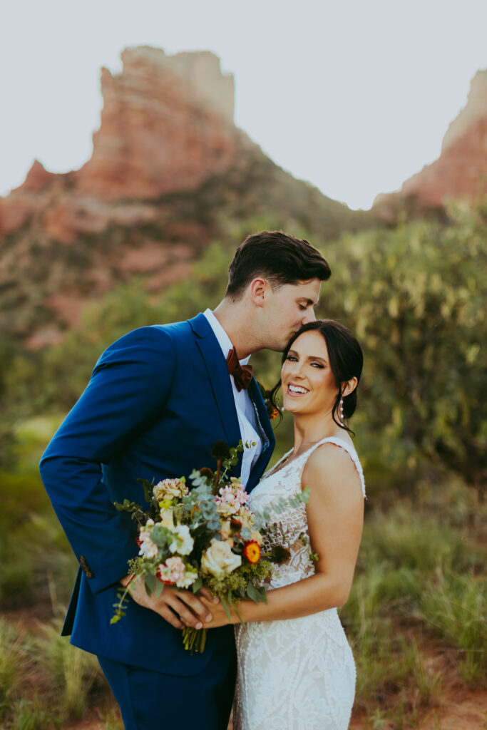 groom kisses bride on the head as they pose for bridal photos in sedona arizona