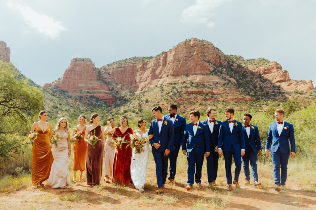 bride and groom look lovingly into each others eyes as their bridal party walks with them at their sides with beautiful sedona red rocks in the backdrop