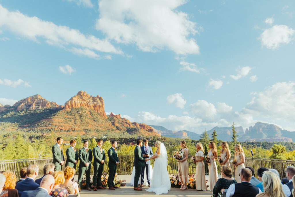 bride and groom hold hands at their wedding ceremony while bridal party looks on with beautiful sedona red rock valley in the backdrop