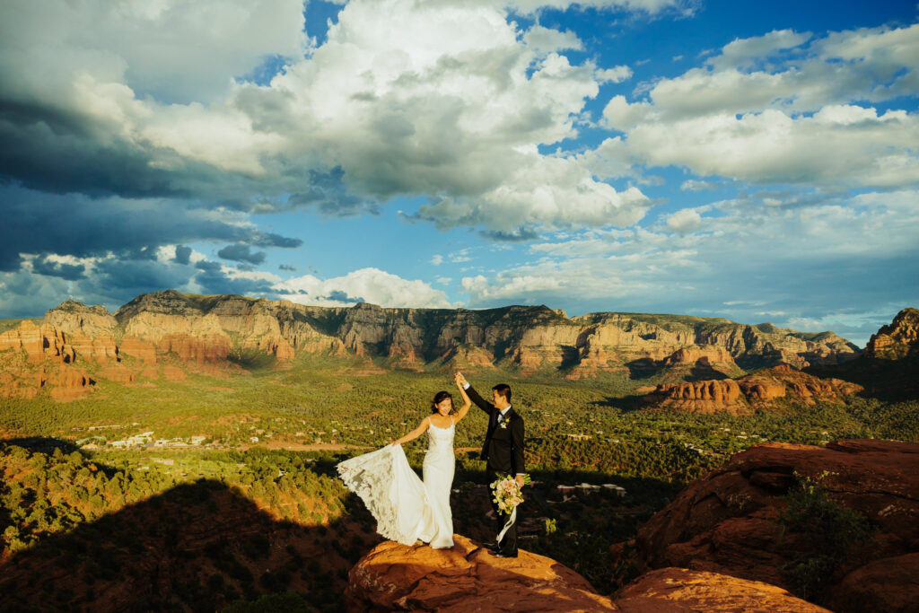 groom spins bride on a lone rock before a beautiful valley in sedona arizona beneath a beautiful blue sky