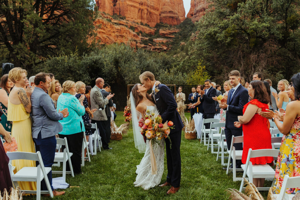 bride and groom kiss while holding each other after their wedding ceremony beneath red rocks at enchantment resort